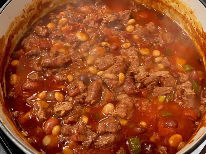 A large pot of hearty beef and bean chili simmering on the stove, showing rich red color and texture