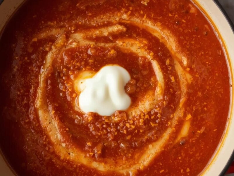 A pot of rich red roasted tomato soup with a swirl of cream on top