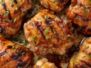 Grilled marinated chicken thighs with charred edges and visible herbs and spices